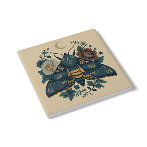 Square ceramic coaster, 4x4 inches, with cork backing. Cream tile features a luna-style moth with crescent moon and botanical florals in teal, blue, and gold. Smooth printed surface; clean, flat illustration. Celestial moth coaster for witchy, cottagecore décor and gifting. Square ceramic drink coaster with cork base, luna moth and moon design.
