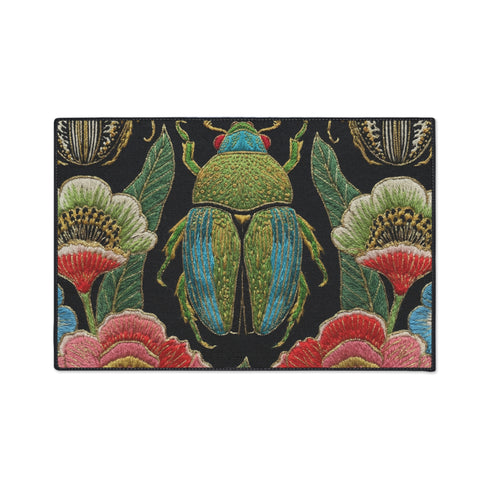 A rectangular doormat featuring a high-fidelity faux embroidery print on a solid black background. The central design is a large, detailed green and teal scarab beetle. It is surrounded by vibrant, flat-printed botanical motifs including large pink, red, and light blue flowers, green foliage, and pale gold-toned seed pods. The mat features a black fabric trim around the edges. The colorful print creates a 2D trompe-l'œil illusion of raised tapestry needlework on a smooth polyester surface.