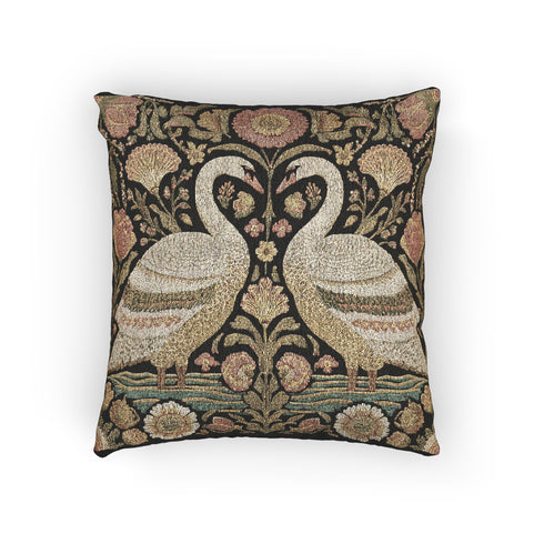 A square decorative throw pillow by Grimoire and Goblet featuring a woven jacquard tapestry design. The pattern displays two regal white swans facing each other with curved necks forming a heart shape, set against a dark background rich with intricate floral botany in beige, dusty rose, and sage green tones. The texture is thick and fabric-like, mimicking vintage needlepoint or Arts and Crafts style. The pillow is stuffed and sewn shut without a visible zipper.