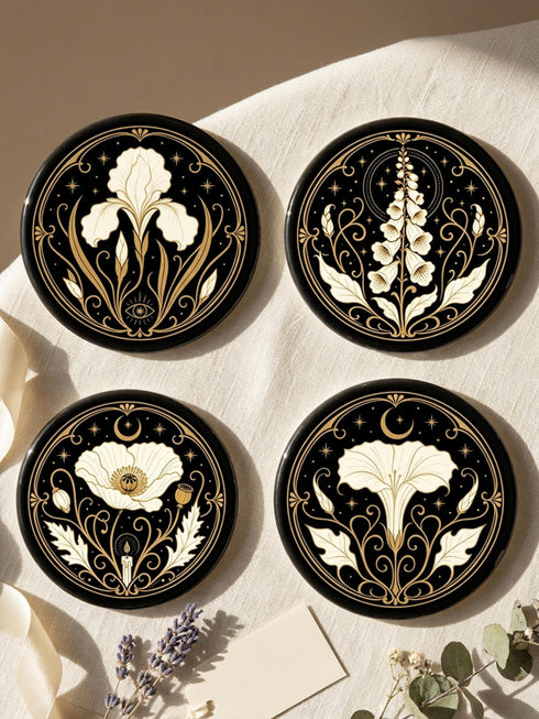 A set of four round 4-inch ceramic coasters featuring a glossy 2D flat-printed Art Deco botanical design. Each coaster displays a different cream-colored flower including a moonflower, foxglove, poppy, and iris, set against a solid black background. The floral motifs are framed by intricate gold linework, crescent moons, four-pointed stars, and mystical symbols like a candle and an all-seeing eye. The coasters have a smooth white edge and are finished with a natural brown cork backing.