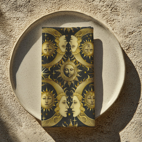 Set of four black cloth napkins with a repeating pattern of golden sun and moon faces, surrounded by swirling flames, craters, and scattered stars.