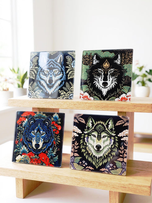 Set of 4 square tempered glass coasters featuring a mystical wolf design on a black background. High-gloss finish with non-slip rubber feet. Dark Academia and Whimsigoth aesthetic home decor. Close-up detail shows grey wolf fur texture and amber eyes. Durable drinkware protection for wooden tables. Grimoire and Goblet gothic luxury barware accessory for coffee tables and desks. Heat resistant glass surface with polished edges.