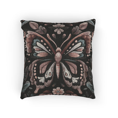 A square decorative pillow featuring an intricately detailed butterfly design in rose pink, blush, and silver-grey colors against a black background. The butterfly is surrounded by botanical elements with symmetrical floral patterns.