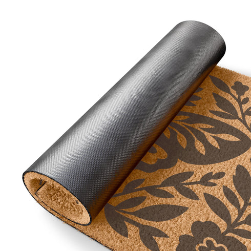 A rectangular, natural brown coir doormat with a coarse, tufted texture. The design is printed in solid black ink in a folk-art, block-print style. In the center is a large, stylized death's-head moth with intricate patterns on its wings. Above the moth is a central all-seeing eye with radiating lashes. The entire central image is enclosed by a symmetrical botanical frame of stylized flowers, stems, and leaves, creating a decorative border. The doormat has a non-slip black vinyl backing.