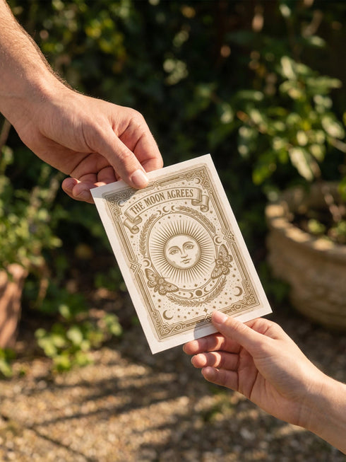 Grimoire and Goblet greeting card featuring a vintage woodcut style illustration of a radial sun with a serene human face. The sun is flanked by two Luna moths and sits above a Triple Moon symbol. A banner above reads THE MOON AGREES in gothic font. Printed in burnished gold tones on cream paper. Interior text reads Yours in this lifetime and the next. Dark Academia and Whimsigoth aesthetic stationery 5x7 card with matching envelope for gothic romance or altar decor.