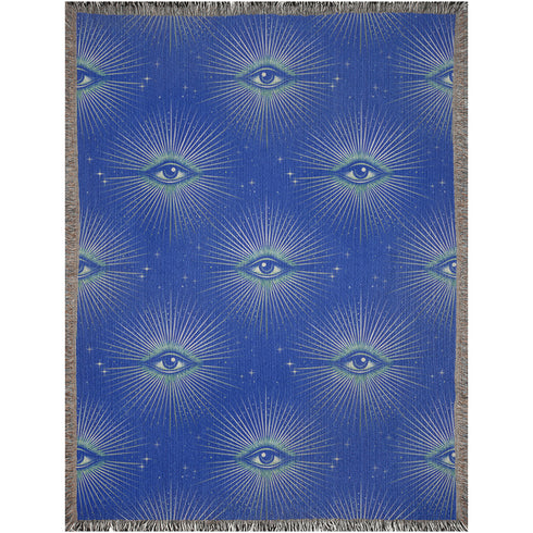 Woven cotton throw blanket with a deep blue background featuring a repeated pattern of all-seeing eyes in gold and seafoam green. The blanket has a colorful fringed edge.