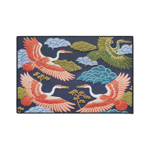 Grimoire and Goblet chinoiserie flying crane faux embroidery doormat featuring three cranes in coral blush and jade green soaring across deep navy background with teal scalloped clouds golden bonsai branches and olive foliage. Printed polyester entryway mat with non-slip rubber backing and black trim. Available 24x18 and 36x24 inches. Asian inspired Japanese crane design housewarming gift home decor