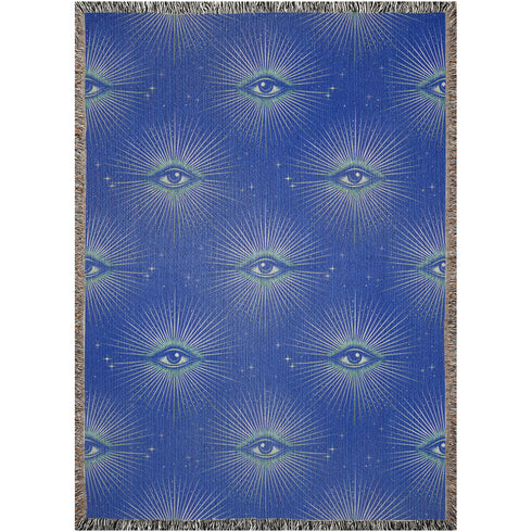 Woven cotton throw blanket with a deep blue background featuring a repeated pattern of all-seeing eyes in gold and seafoam green. The blanket has a colorful fringed edge.