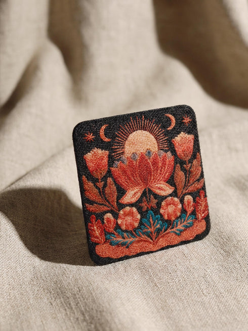 A Grimoire and Goblet drink coaster featuring a rustic faux burlap texture print. The coaster displays a gothic botanical design in dark charcoal ink on a tan jute-like polyester background. The smooth fabric surface mimics a woven look. Ideal for Dark Academia decor and protecting tables from spills. The design includes a central motif with vintage styling.