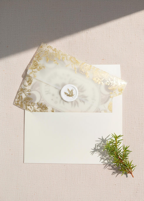 a luxury Grimoire and Goblet ritual card set. A 5x7 cream-colored folded card features an intricate, art-nouveau-style gold foil illustration of a Juniper plant, with the words "Juniper: Cleansing & Fortune." The card is presented with a translucent vellum envelope, which has a gold floral border and a white adhesive wax seal. Inside, the card reveals a vellum-wrapped keepsake, which unfurls to a 4x6 ritual card printed on thick, 160 GSM handmade cotton paper with a rough, deckled edge.