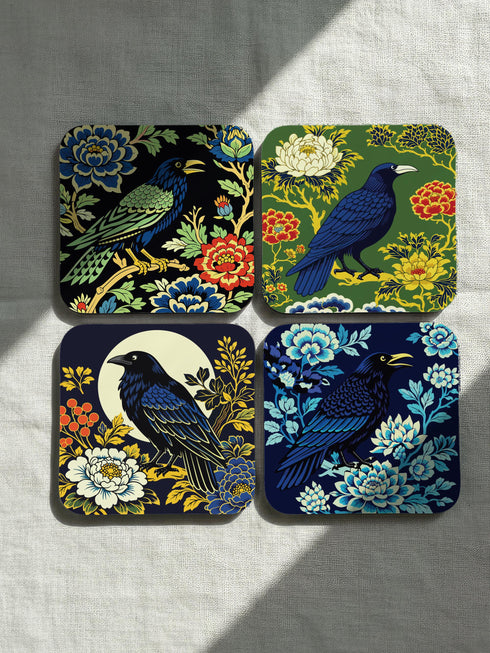 Grimoire and Goblet set of 4 glossy square coasters featuring Chinoiserie style raven illustrations. 1: Navy blue with blue floral pattern and raven. 2: Navy background with black raven, white full moon, and red berries. 3: Moss green background with blue bird and yellow chrysanthemums. 4: Black background with teal-winged raven and red peonies. MDF hardboard with cork backing. Flat vector botanical art style.