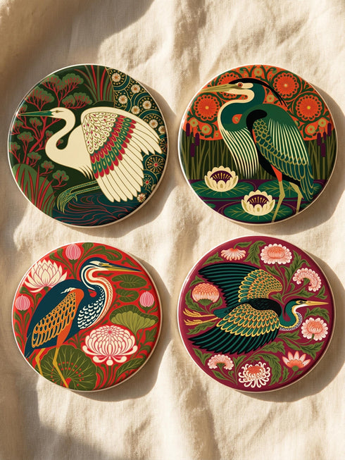 This set of four round ceramic coasters features a glossy, smooth, high-fidelity flat-printed surface. Each piece displays highly detailed Art Nouveau style illustrations of herons and egrets surrounded by stylized water lilies, chrysanthemums, and rich foliage. The vibrant, intricate color palette includes deep emerald greens, rich crimson reds, navy blues, and golden yellows. The sides are smooth, unprinted white ceramic, and the underside is fitted with a natural brown cork backing.