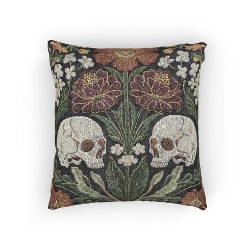 A Grimoire and Goblet woven tapestry pillow featuring a symmetrical dark botanical design. Two beige human skulls face each other in profile against a dark charcoal background. They are surrounded by deep burgundy dahlia flowers, sage green leaves, and small white floral clusters in an Arts and Crafts style. The texture is a visible fabric weave. The design is double-sided, square, and filled.