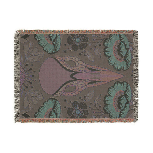 A midnight navy woven cotton blanket featuring a large central raven skull surrounded by rust and ochre flowers, and sage green ferns. Crescent moons are located in the four corners. The blanket has a colorful fringed edge and a textured, loomed appearance. Displayed as a premium gothic botanical home decor piece by Grimoire and Goblet.