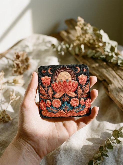 A Grimoire and Goblet drink coaster featuring a rustic faux burlap texture print. The coaster displays a gothic botanical design in dark charcoal ink on a tan jute-like polyester background. The smooth fabric surface mimics a woven look. Ideal for Dark Academia decor and protecting tables from spills. The design includes a central motif with vintage styling.