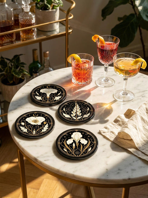 A set of four round 4-inch ceramic coasters featuring a glossy 2D flat-printed Art Deco botanical design. Each coaster displays a different cream-colored flower including a moonflower, foxglove, poppy, and iris, set against a solid black background. The floral motifs are framed by intricate gold linework, crescent moons, four-pointed stars, and mystical symbols like a candle and an all-seeing eye. The coasters have a smooth white edge and are finished with a natural brown cork backing.
