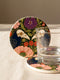 A square drink coaster with a high-gloss finish and natural cork backing. The centralized, symmetrical design features two detailed, cream-colored avian bird skulls facing inward. They are framed by lush botanical flora, including a large purple flower, blush pink blooms, rust-red roses, and green ferns, all set against a deep navy blue background with gold linework accents. Functional gothic, whimsigoth, and dark academia drinkware designed by the Grimoire and Goblet brand.