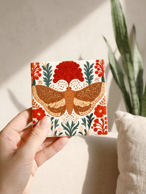 A detailed close-up of a luxury ceramic mug and matching square coaster set from Grimoire and Goblet. The items feature a vintage-style scientific illustration of a large moth with intricate wing patterns in earth tones of rust red and moss green, resting on stylized botanical foliage. The aesthetic is Dark Academia and Victorian Gothic. The mug is a large 15oz white ceramic vessel with a sturdy C-handle. The coaster is a glazed ceramic tile with a glossy finish.