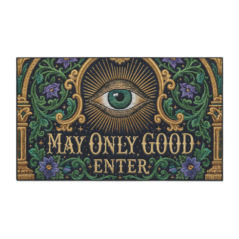 Rectangular doormat printed on a deep black ground with a faux embroidery effect that imitates antique crewelwork. A large green eye sits at the center within an antique gold radial sunburst, with ornate gold serif lettering below reading MAY ONLY GOOD ENTER. Green acanthus leaf scrollwork and antique gold architectural columns run along the borders, accented with small five petaled purple flowers. A sleek black trim frames all four edges of the flat printed surface.