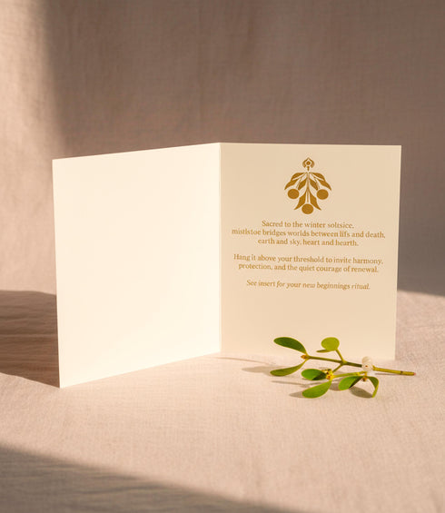 A Grimoire & Goblet luxury Mistletoe ritual card set. The 5x7 cream greeting card features gold celestial designs framing “Mistletoe” and “Love, Protection & New Beginnings.” Shown with a vellum wrap printed in gold florals, a white wax seal with mistletoe, and a premium envelope. Includes a 4x6 ritual insert on handmade deckled paper titled “Ritual for Peace and Protection.” A spiritual Yule stationery set designed as a luxurious unboxing experience.