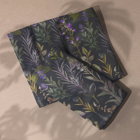 Set of four dark charcoal cloth napkins with a repeating pattern of muted purple, green, and gold herbs and flowers in an elegant botanical design.
