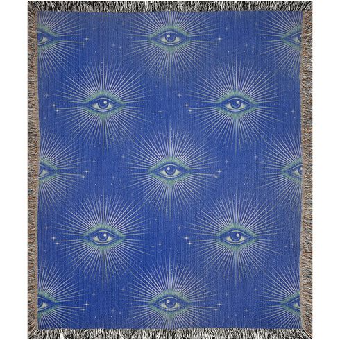 Woven cotton throw blanket with a deep blue background featuring a repeated pattern of all-seeing eyes in gold and seafoam green. The blanket has a colorful fringed edge.