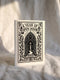 A vertical 5x7 inch pearlescent greeting card by Grimoire and Goblet featuring a high-contrast black woodcut-style illustration. The design centers on a gothic cathedral archway framing a glowing candle and a winding path leading forward. Surrounding the arch are intricate floral vines and stars. A banner at the top reads A YEAR OF OPEN DOORS in serif typography. The paper has a subtle silvery shimmer. The inside contains a printed poem about warmth and promise. Perfect for spiritual gifting.