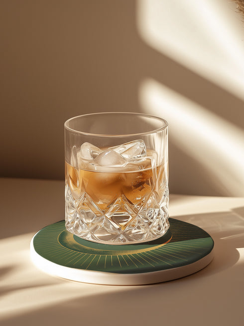 Round ceramic coaster with forest green background. Golden crescent moon embraces a sun at the center. Fine golden lines radiate outward, creating a sunburst pattern to the edge. White rim indicates cork backing. Coaster diameter is 4.04 inches.