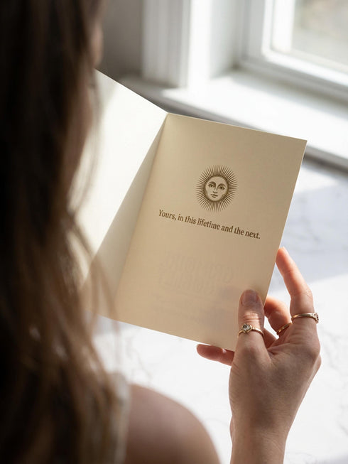 Grimoire and Goblet greeting card featuring a vintage woodcut style illustration of a radial sun with a serene human face. The sun is flanked by two Luna moths and sits above a Triple Moon symbol. A banner above reads THE MOON AGREES in gothic font. Printed in burnished gold tones on cream paper. Interior text reads Yours in this lifetime and the next. Dark Academia and Whimsigoth aesthetic stationery 5x7 card with matching envelope for gothic romance or altar decor.