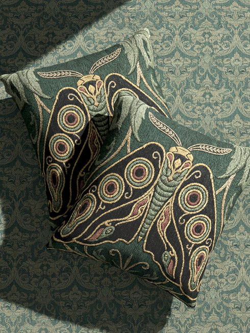 A Grimoire and Goblet heirloom woven pillow featuring a large, symmetrical Art Nouveau Emperor Moth design. The moth is woven in textured threads of midnight black, burnished gold, and rust terracotta against a deep sage forest green background. Four prominent eye-spot patterns adorn the wings, framed by stylized botanical acanthus leaves in the upper corners. Double-sided tapestry fabric with a rich, tactile surface. No printed ink; purely woven structure.