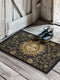 Handcrafted celestial doormat featuring an antique gold sun face with knowing eyes, surrounded by botanical motifs against a deep charcoal background with elegant black trim.