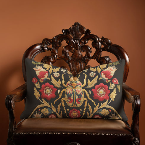 A rectangular black lumbar pillow with a premium linen-feel texture. The pillow features a detailed, tapestry-style Art Nouveau print of a large scarab beetle at its center. The beetle and surrounding symmetrical floral and botanical motifs are rendered in rich colors of antique gold, deep crimson red, and muted teal. This ornate, maximalist design is set against a dark charcoal black background, creating a moody, gothic, & scholarly aesthetic suitable for dark academia or victorian home decor.