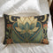 Lotus Lumbar Premium PillowA rectangular lumbar pillow in a dark, moody Art Nouveau style. The design features a large, central lotus flower in cream and teal, set against a deep navy blue background. The lotus is framed by intricate, flowing golden lines characteristic of the Art Nouveau period. On either side of the central flower are golden crescent moons and small stars, creating a celestial theme. The pillow has a visible, tactile texture that resembles a vintage linen or tapestry fabric.