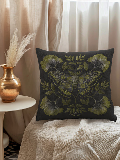 A square decorative pillow featuring an intricately detailed Luna moth in sage green and olive tones on a black background. The moth is centered in a symmetrical arrangement with ginkgo-like leaves and botanical elements surrounding it.