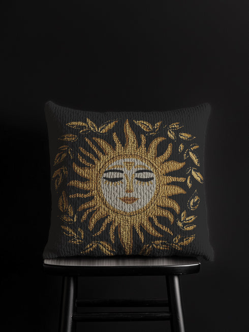 Black woven throw pillow with golden embroidered sun and laurel design, featuring a serene celestial face with closed eyes.