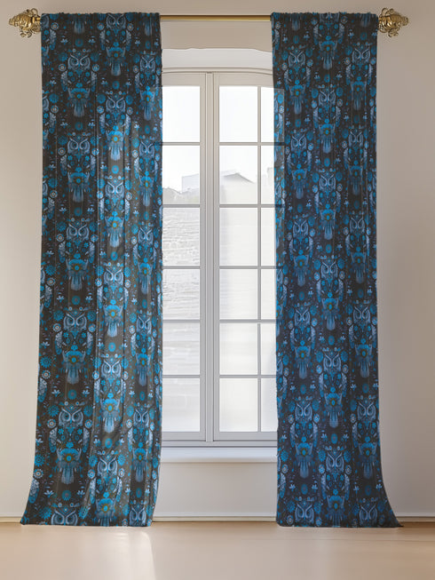 A sheer curtain panel featuring a repeating pattern of stylized owls in luminous blue tones, surrounded by delicate botanical flowers and flourishes on a dark background.