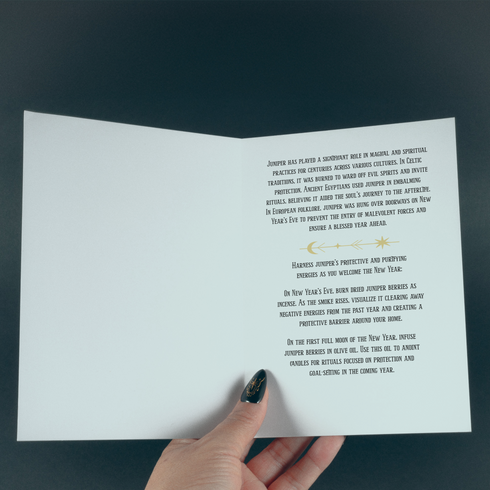 Juniper-themed greeting card featuring a gold design on a black background with celestial and botanical motifs. The text reads: 'Protection & Purification.' The inside message explains the magical and spiritual significance of juniper, including rituals for New Year's Eve and the first full moon, focusing on protection and purification practices.