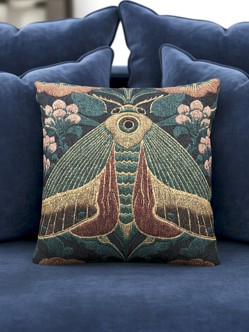 A Grimoire and Goblet woven tapestry pillow featuring a large, symmetrical Oleander Hawk Moth design. The moth has ochre and rust-colored wings with a distinct central eye marking on the thorax. It is set against a deep petrol teal background and flanked by stylized Arts and Crafts floral patterns in dusty rose and sage green. The texture is thick and woven, not printed, showcasing intricate thread details.