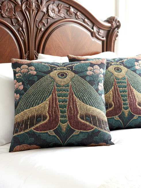 A Grimoire and Goblet woven tapestry pillow featuring a large, symmetrical Oleander Hawk Moth design. The moth has ochre and rust-colored wings with a distinct central eye marking on the thorax. It is set against a deep petrol teal background and flanked by stylized Arts and Crafts floral patterns in dusty rose and sage green. The texture is thick and woven, not printed, showcasing intricate thread details.