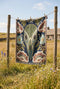 A midnight navy woven cotton blanket featuring a large central raven skull surrounded by rust and ochre flowers, and sage green ferns. Crescent moons are located in the four corners. The blanket has a colorful fringed edge and a textured, loomed appearance. Displayed as a premium gothic botanical home decor piece by Grimoire and Goblet.