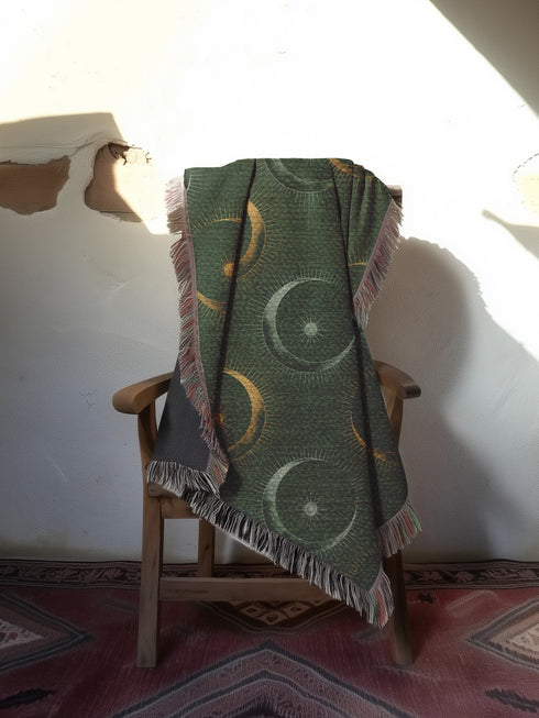 Forest green cotton throw blanket with woven silver moon phases and golden sun motifs, finished with multicolored fringe trim.