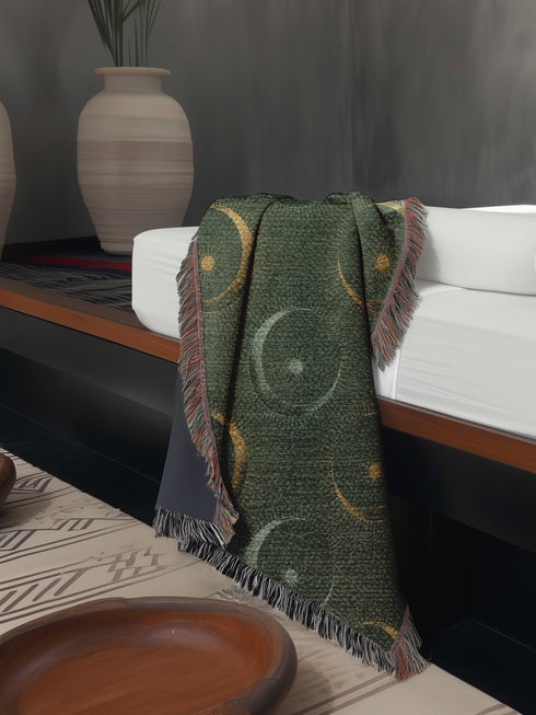 Forest green cotton throw blanket with woven silver moon phases and golden sun motifs, finished with multicolored fringe trim.