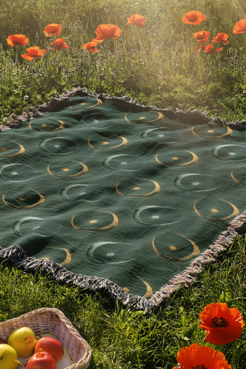 Forest green cotton throw blanket with woven silver moon phases and golden sun motifs, finished with multicolored fringe trim.