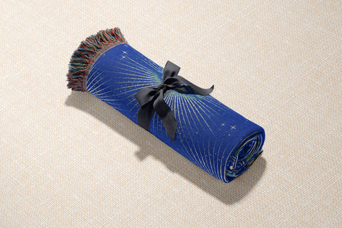 Woven cotton throw blanket with a deep blue background featuring a repeated pattern of all-seeing eyes in gold and seafoam green. The blanket has a colorful fringed edge.