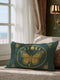 A rectangular lumbar pillow cover, measuring 20 by 12 inches, is displayed against a neutral background. The pillow cover is made of a deep teal green fabric with a subtle, linen-like texture. In the center, a large, intricately detailed butterfly with spread wings is printed in a shimmering gold color. The butterfly is framed by a golden oval which also contains a series of gold moon phase symbols, showing the full lunar cycle. The four corners of the pillow is adorned with gold floral design.