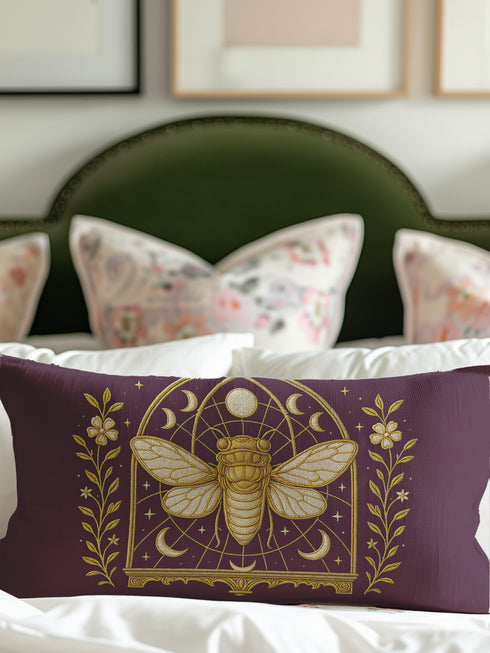 A rectangular lumbar pillow cover in a deep, moody plum-purple. The pillow features a detailed, symmetrical design in a shimmering gold color. In the center is a large, ornate cicada with translucent, veined wings, facing forward. The cicada is framed by a gothic-style archway with intricate patterns. Above the arch is a full moon, flanked by waxing and waning crescent moon phases. The design is bordered by vertical botanical vines with small flowers and stars, completing the mystical aesthetic.