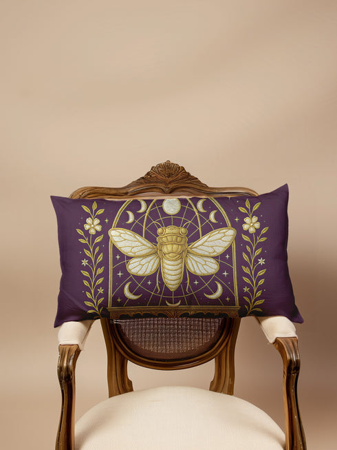 A rectangular lumbar pillow cover in a deep, moody plum-purple. The pillow features a detailed, symmetrical design in a shimmering gold color. In the center is a large, ornate cicada with translucent, veined wings, facing forward. The cicada is framed by a gothic-style archway with intricate patterns. Above the arch is a full moon, flanked by waxing and waning crescent moon phases. The design is bordered by vertical botanical vines with small flowers and stars, completing the mystical aesthetic."