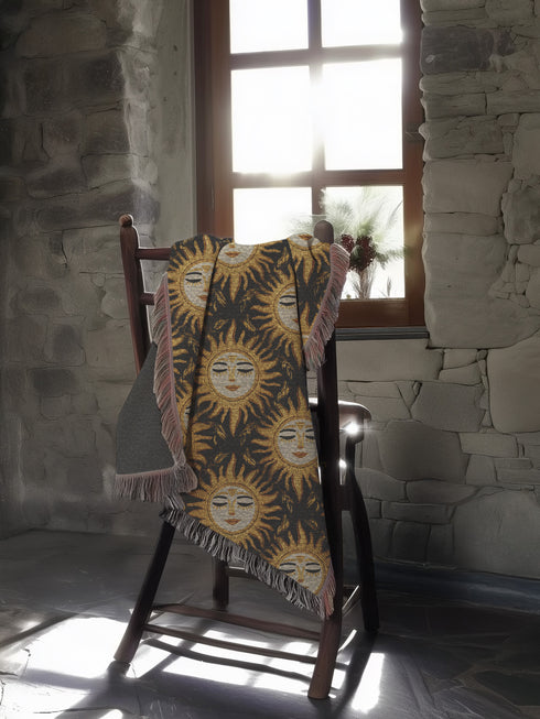 A woven cotton throw featuring a celestial sun face pattern in gold and black tones, framed by soft fringe.
