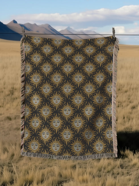 A woven cotton throw featuring a celestial sun face pattern in gold and black tones, framed by soft fringe.