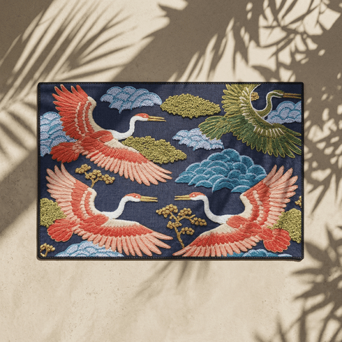 Grimoire and Goblet chinoiserie flying crane faux embroidery doormat featuring three cranes in coral blush and jade green soaring across deep navy background with teal scalloped clouds golden bonsai branches and olive foliage. Printed polyester entryway mat with non-slip rubber backing and black trim. Available 24x18 and 36x24 inches. Asian inspired Japanese crane design housewarming gift home decor
